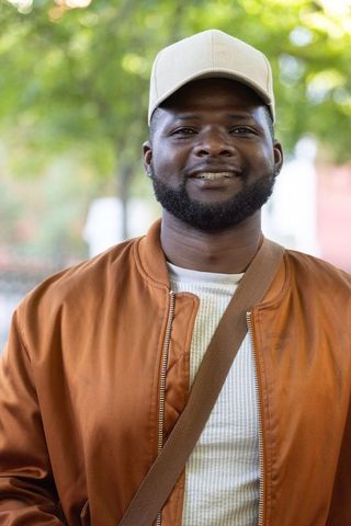 Smiling african man in beige cap and copper bomber jacket, urban portrait with crossbody