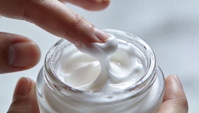Dipping fingertip into moisturizer jar showing rich elastic cream texture