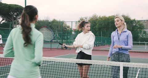 Female tennis coach leading group drills with players on outdoor hard court