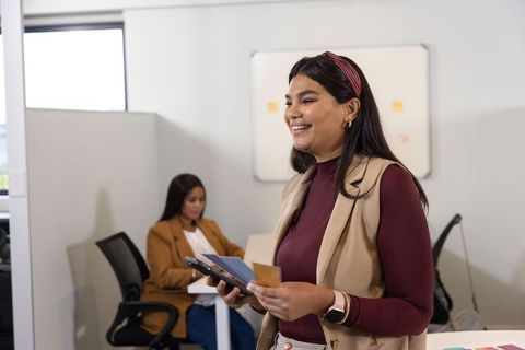 Female leader presenting in modern office, holding smartphone and notes, smiling and engaging team