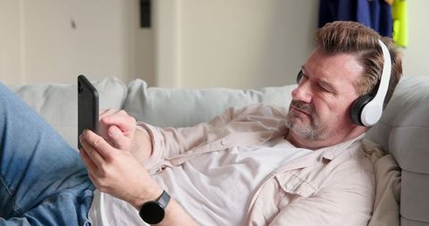 Relaxed man using tablet with headphones on sofa