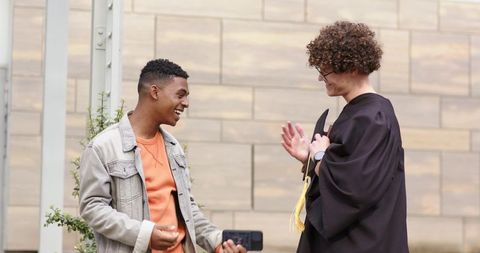 Graduation celebration: diverse friends recording graduate in gown with yellow tassel