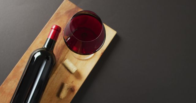 Red wine glass, bottle and cork lying on wooden board with copy space on black background. Wine, alcohol, beverage and wine tasting concept.
