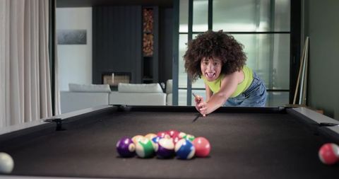 African american woman leaning over pool table aiming cue showing excited home leisure