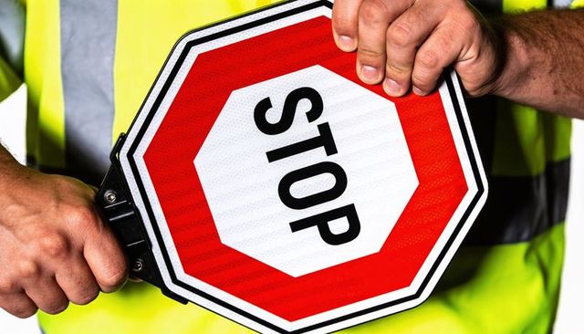 Holding reflective stop sign wearing high-visibility vest close-up for traffic control