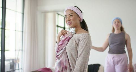 African american woman trying on silk scarf while friend smiles in bright cozy home