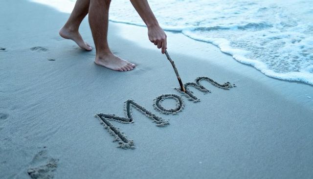 Writing mom in wet sand on beach by barefoot man with incoming waves