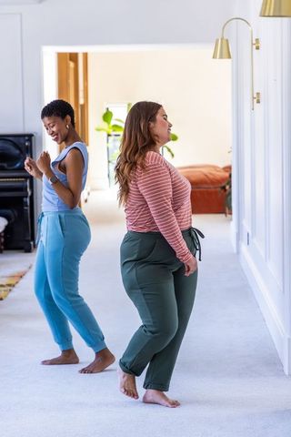 Two diverse women dancing barefoot in bright home hallway, relaxed lifestyle moment