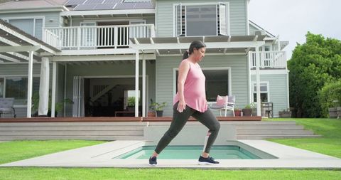Mature asian woman doing lunges beside backyard pool on suburban deck for home fitness