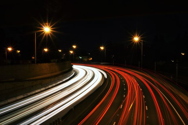 Light trails of cars on a highway captured with long exposure, showcasing city movement at night. Useful for themes related to urban lifestyle, transportation infrastructure, motion and dynamics, night travel, and city nightlife.