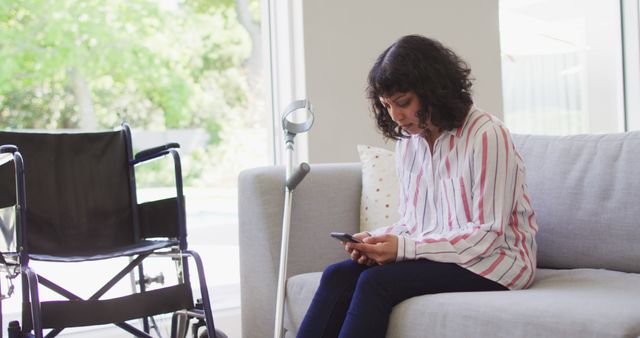 Woman Using Smartphone in Living Room with Wheelchair Nearby - Download Free Stock Images Pikwizard.com