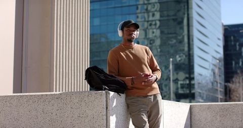 African American Man Leaning on Ledge Listening to Music in Urban Plaza