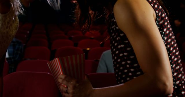 Friends exchanging popcorn in a dark movie theater. Ideal for illustrating movie-going experiences, friendship moments, group outings, entertainment-related articles, and social media posts about movie nights.