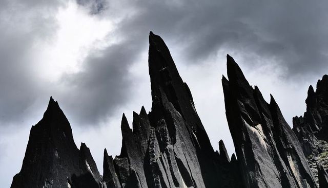 Rising jagged rock spires cutting brooding sky with vertical grooves and alpine lichen