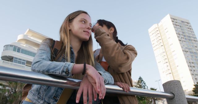 Teen Girls Outdoors Sharing Secret Leaning on Railing in Cityscape - Download Free Stock Images Pikwizard.com