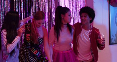 Multicultural Friends Celebrating Birthday Party With Tinsel Backdrop and Colorful Lights