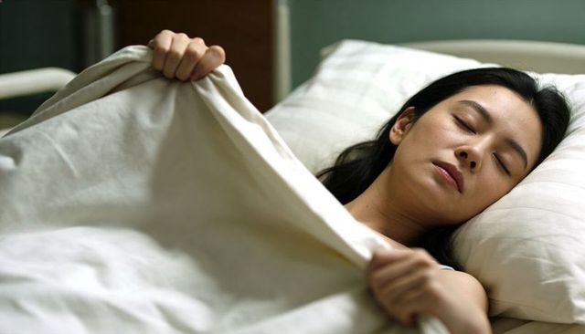 Sleeping asian woman gripping duvet resting on bed, serene restful sleep, minimalist bedroom