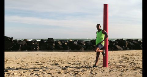 Jogger adjusting arm band on beach near rocky shoreline