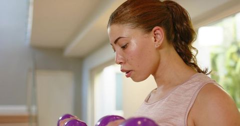 Woman starting dumbbell workout at home with focused form in sunlit minimalist interior