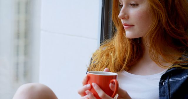 Red-haired woman relaxing by window with coffee mug, enjoying quiet moment - Download Free Stock Images Pikwizard.com