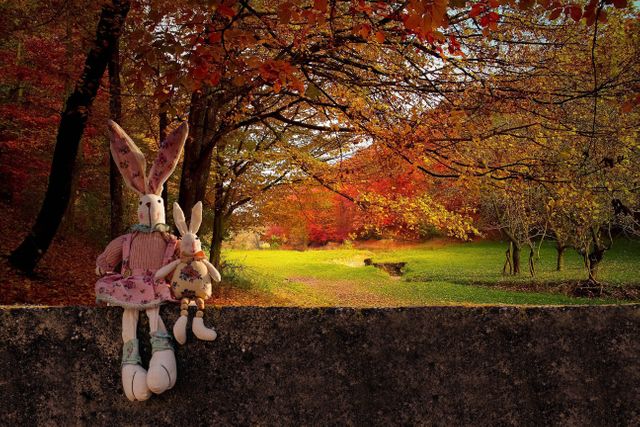 Adorable stuffed rabbits sitting on wall with vibrant fall foliage in the background. Perfect for themes related to childhood, autumn, nature, and outdoor activities. Great for social media, blogs, holiday cards, and seasonal promotions.