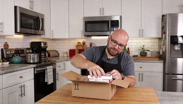 Bald man unboxing cooking kit on kitchen island, home chef preparing new pantry staple
