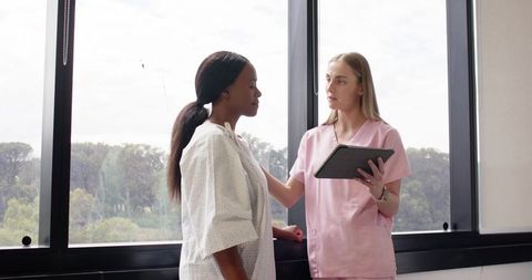 Nurse consulting patient by clinic window holding tablet during outpatient visit