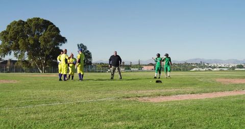 Diverse male baseball teams huddling with umpire on sunny community field showing teamwork
