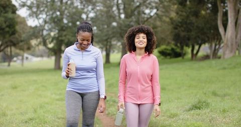 Diverse women walking on park trail in activewear holding water bottles for fitness