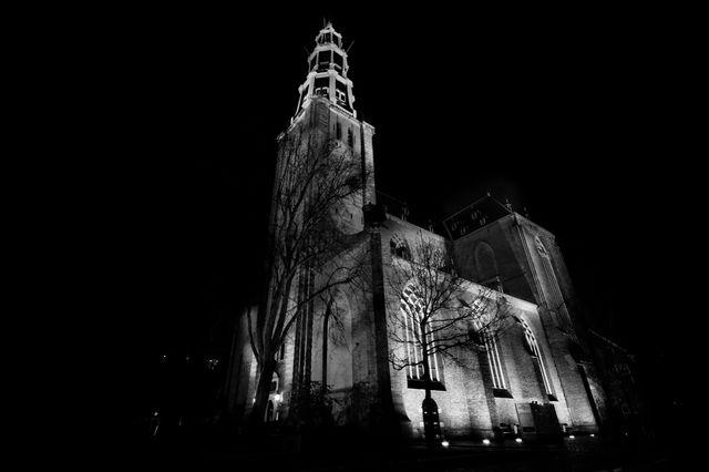Historic church building with gothic architecture illuminated at night. The tower and facade create a dramatic feel in black and white. Possible uses include depicting heritage sites, religious themes, architectural beauty, and mood settings in literature or presentations.