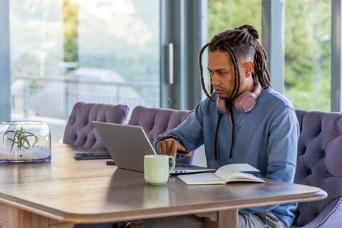 African american man working remotely at home desk with laptop, headphones and notebook