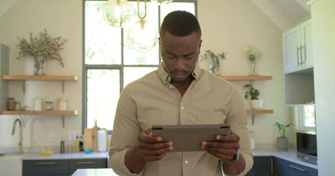 African American Man Using Tablet in Modern Kitchen, Focusing on Home Tasks