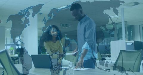 Business partners collaborating over laptop and documents with global map overlay