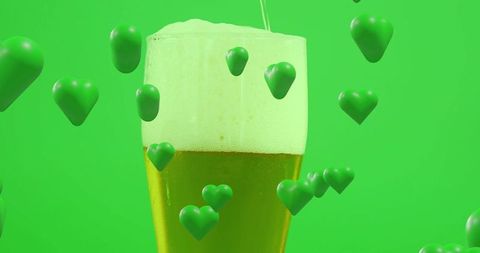 Pouring pint glass of beer with frothy head surrounded by floating green hearts