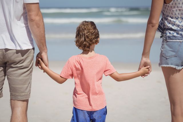 Rear view of boy holding hands while standing with parents at beach