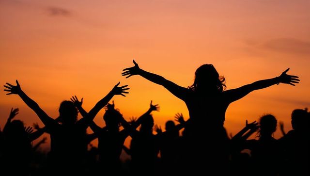 Sunset silhouettes of people raising arms in group celebration and unity