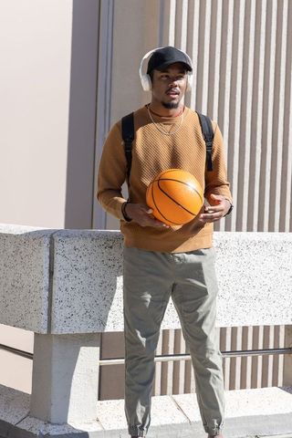 Sunlit african american man holding basketball on rooftop terrace wearing headphones