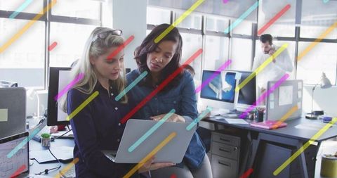 Collaborating professionals reviewing laptop in bright open-plan office with city views