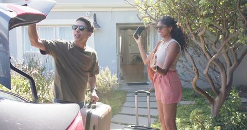African american couple loading luggage into car while smiling and preparing sunny road trip