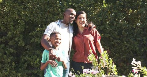 Smiling family enjoying sunlit backyard garden with blooming planters, lush hedge and joyful smiles
