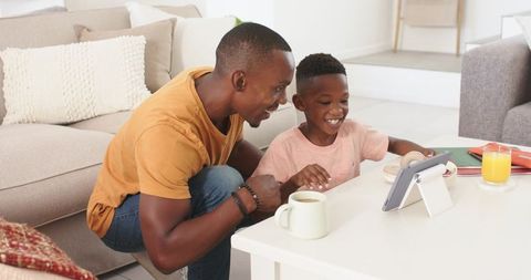 Father guiding son on tablet at home, learning together, smiling parent-child tech bonding