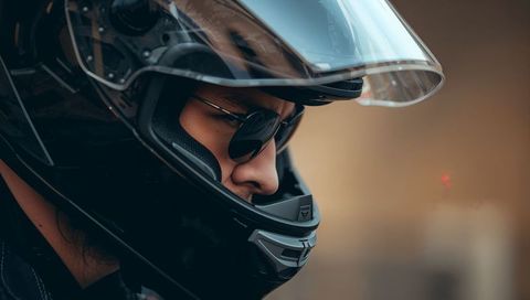 Motorcycle rider wearing glossy black full-face helmet and sunglasses showing left profile