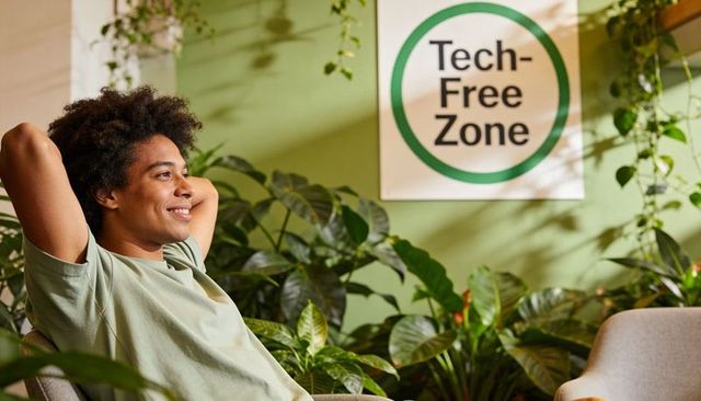 Relaxing young man in green lounge surrounded by plants under tech-free zone sign for digital detox