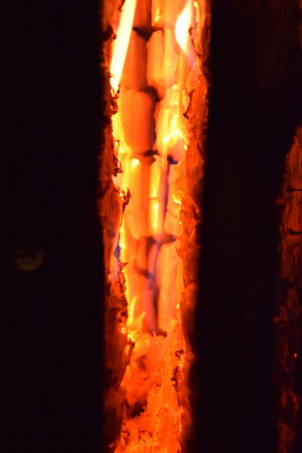 Detailed close-up of wood embers glowing intensely in a dark setting, highlighting the warm orange light and the textures of the wood. Useful for backgrounds, depicting warmth, heat, fire safety materials, or campfire settings.