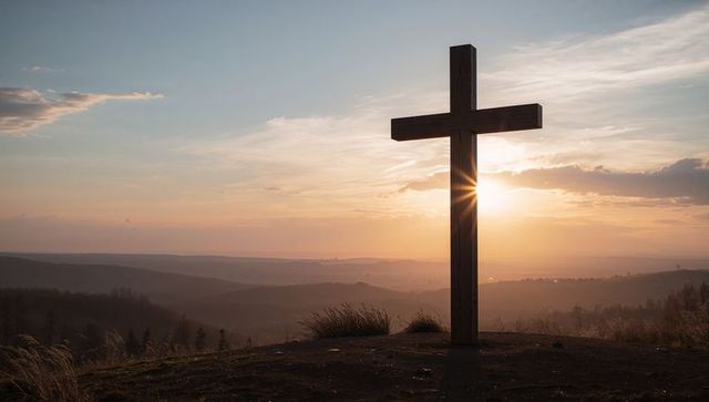 Wooden cross standing on hilltop at sunset with sunburst and misty valley serene silhouette