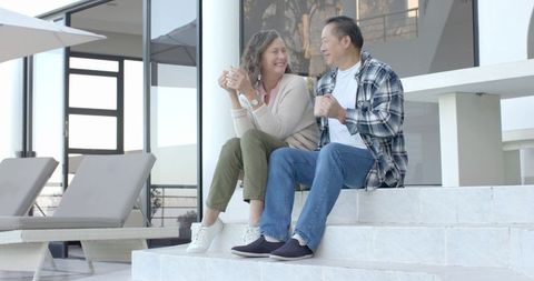 Diverse Senior Couple Relaxing Together on Steps Outside Modern Home