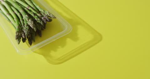Fresh Asparagus in Transparent Container on Yellow Background