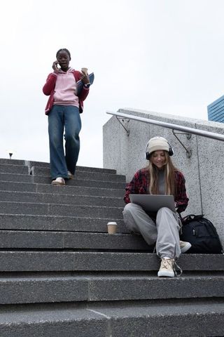 College students on campus steps studying with laptop and talking on phone