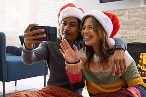 Couple wearing santa hats video calling by fireplace celebrating cozy holiday moments