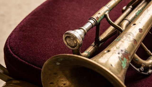 Resting tarnished brass trumpet on maroon velvet cushion with silver mouthpiece